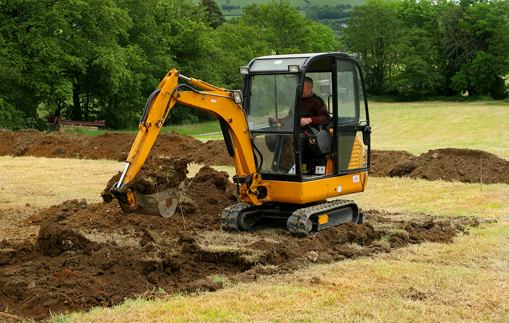 Small excavator working on a grass field — swing drive duty cycles on and off through the shift, classic intermittent orbital application.